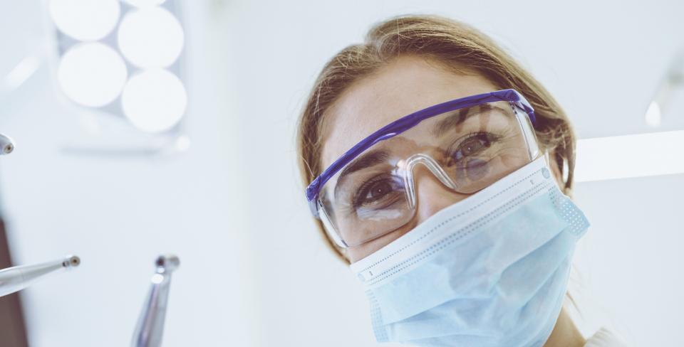 Smiling person wearing surgical mask and holding dental tool